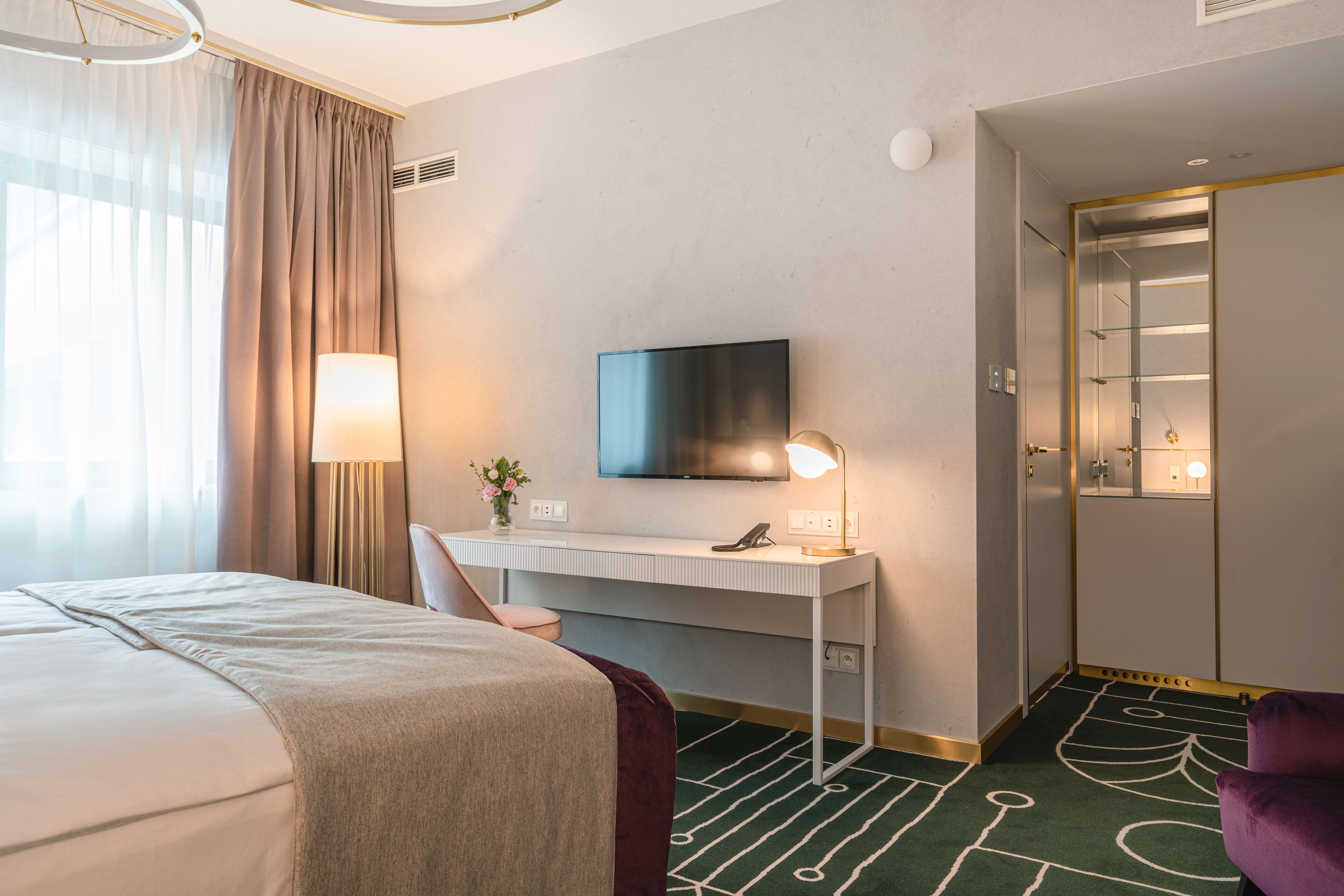 A hotel room with a bed, desk, TV, lamp, and a bathroom with a shower.