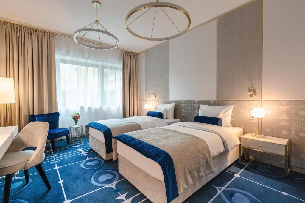 A hotel room with two beds, a desk, a chair, and a small table with a vase of flowers.