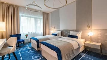 Ein Hotelzimmer mit zwei Betten, einem Schreibtisch, einem Stuhl und einem kleinen Tisch mit Blumen in einer Vase.
