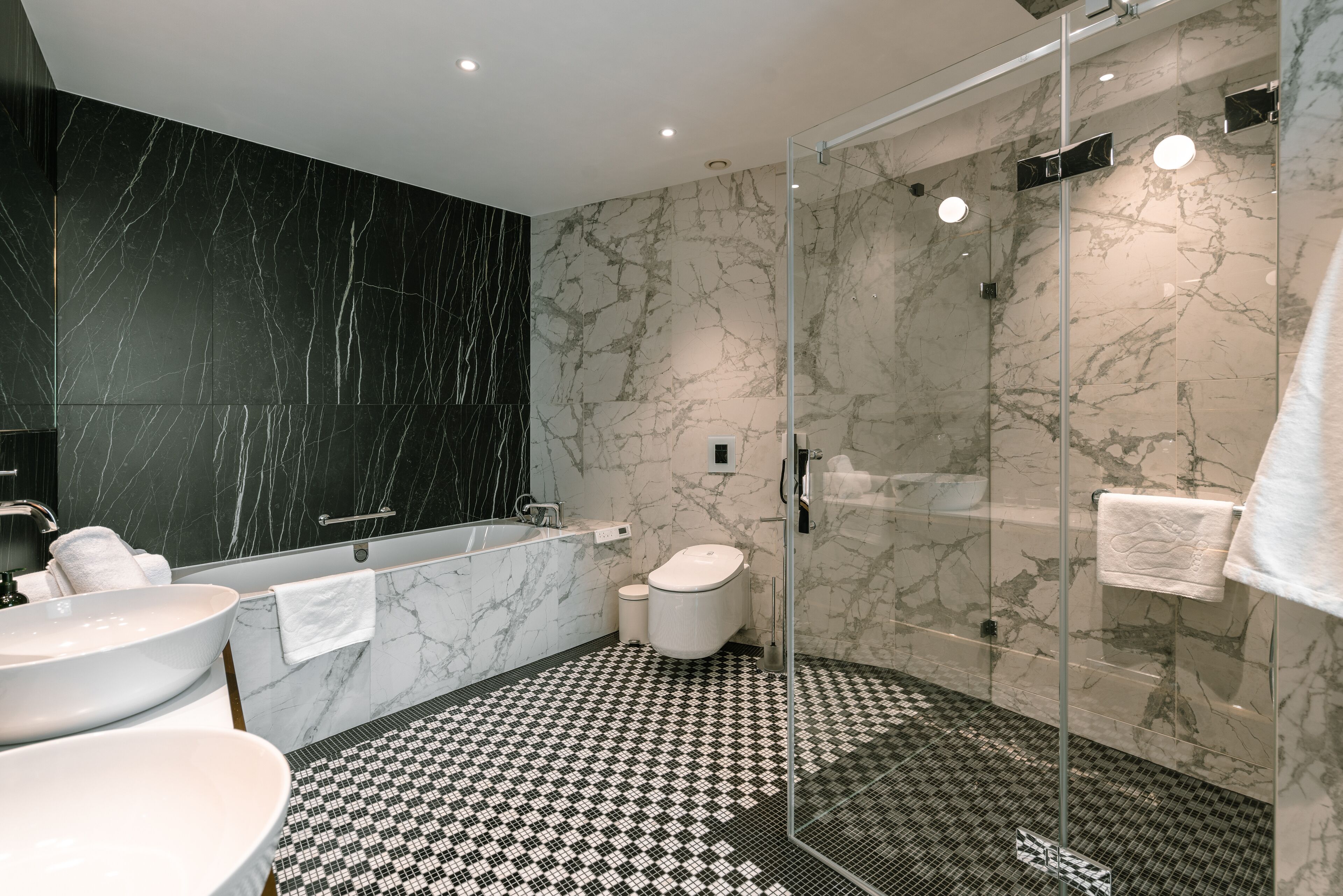 A modern bathroom with a black and white checkered floor, a glass-enclosed shower, a white sink, and a bathtub.