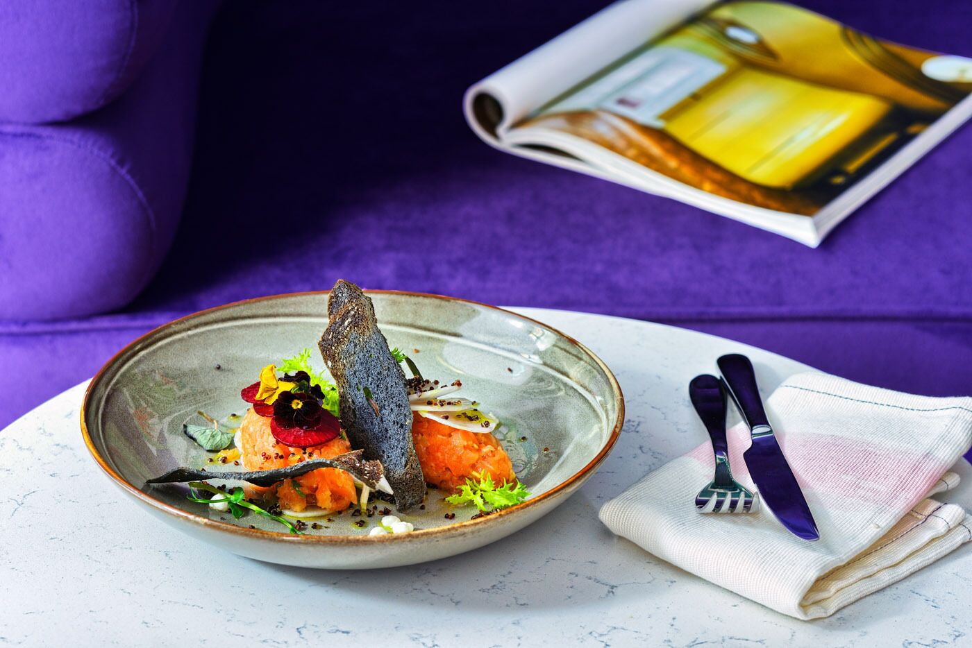 A plate of food with a fish, vegetables, and a decorative element on a white table.