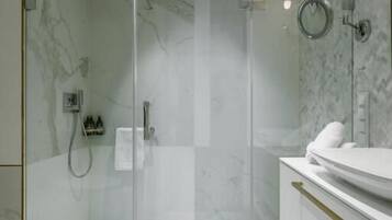 A modern bathroom with a glass-enclosed shower, a white sink, and marble walls.