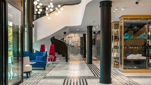 Een moderne lobby met een blauwe bank, rode stoelen, een glazen vitrine en een marmeren vloer.