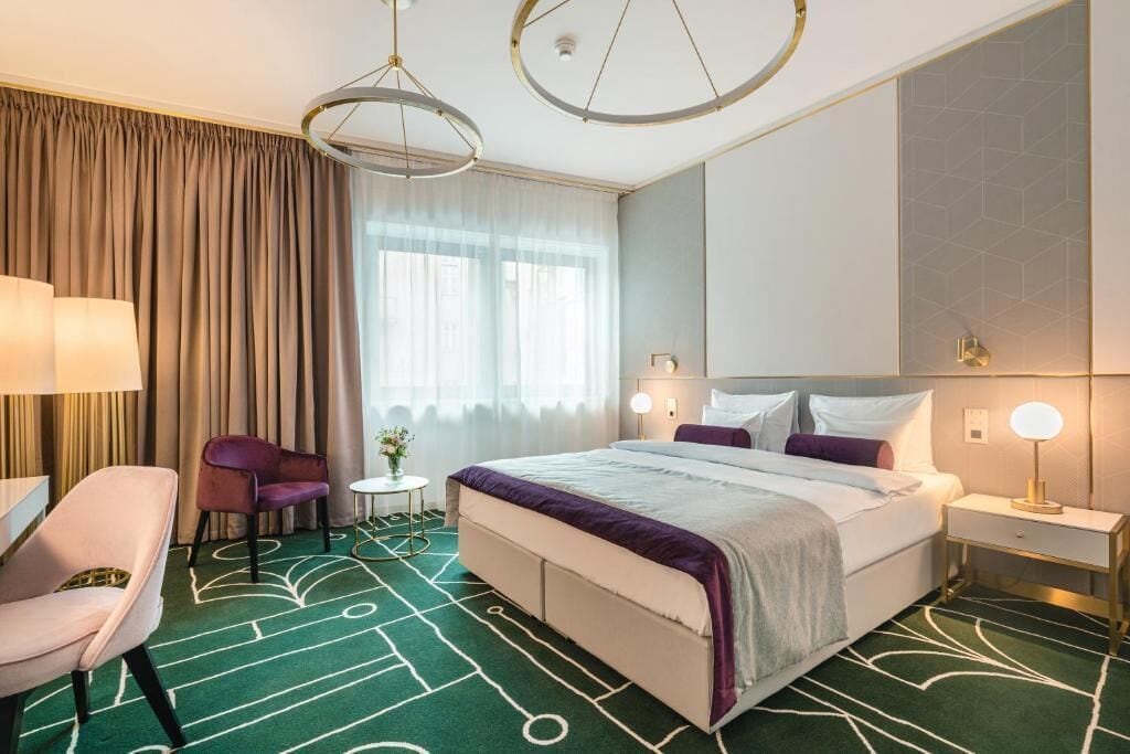 A hotel room with a large bed, a desk, a chair, and a small table.