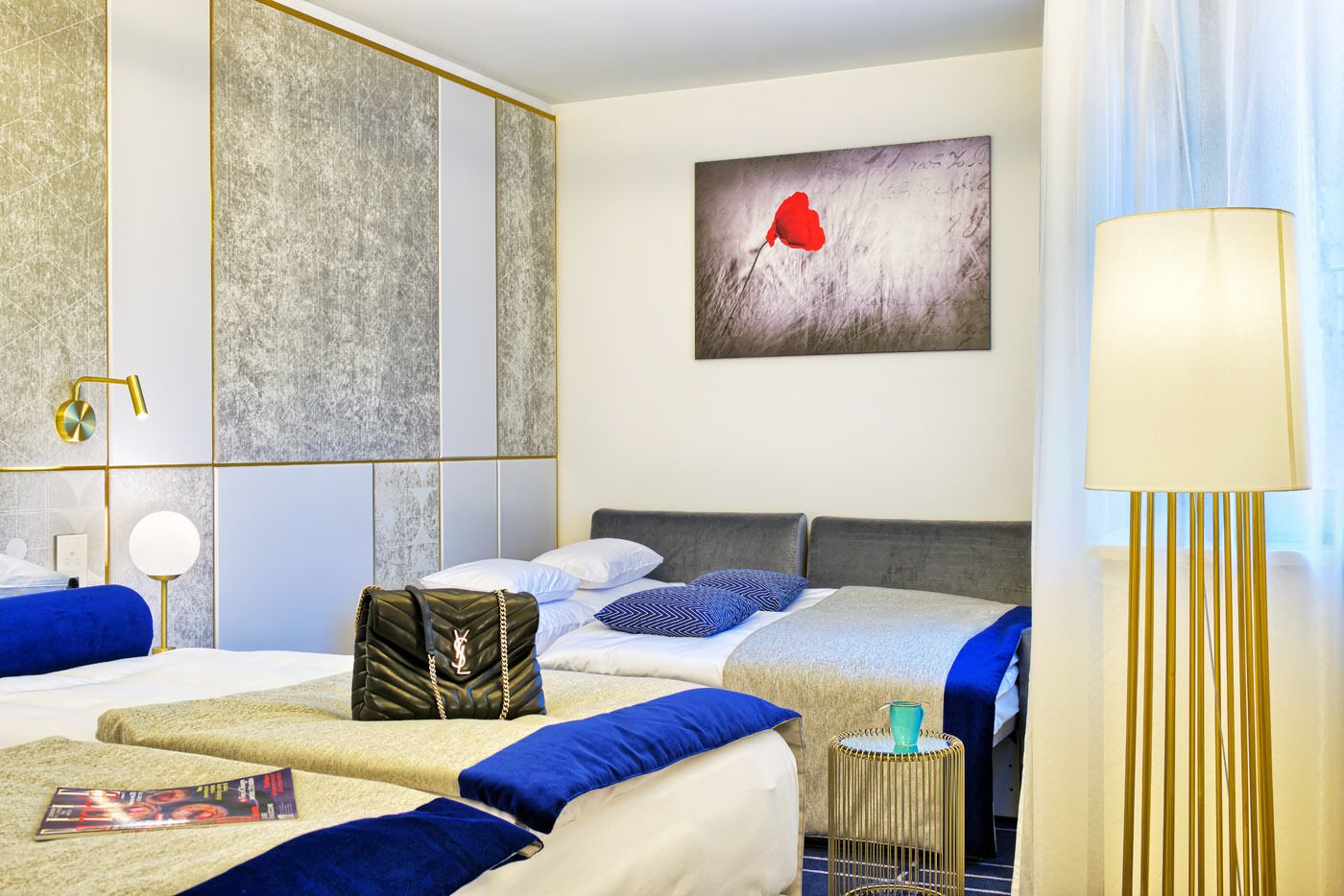 Una habitación de hotel con una cama, mesitas de noche, una lámpara, un cuadro y una maleta.