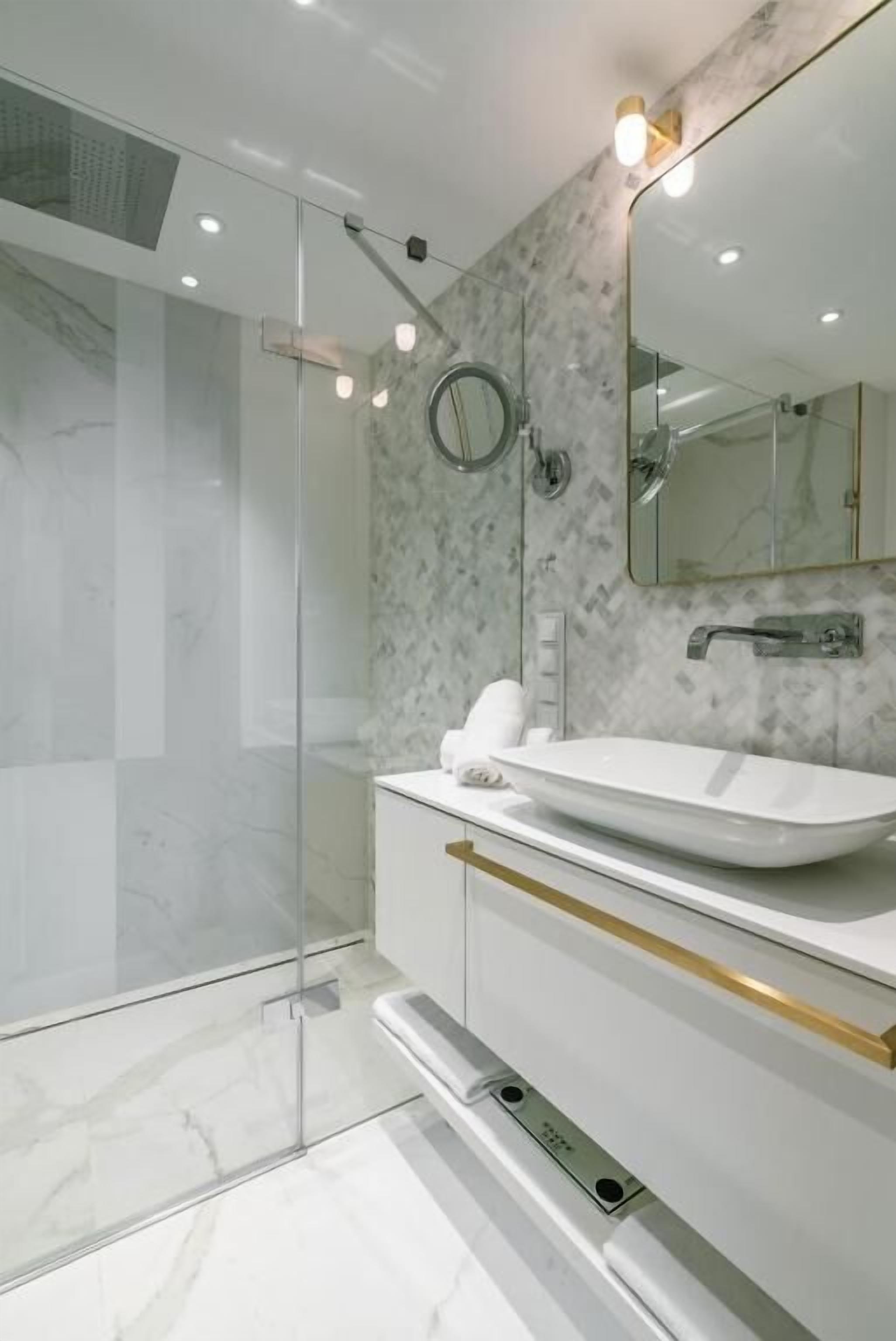 A modern bathroom with a glass-enclosed shower, a white sink, and a marble backsplash.