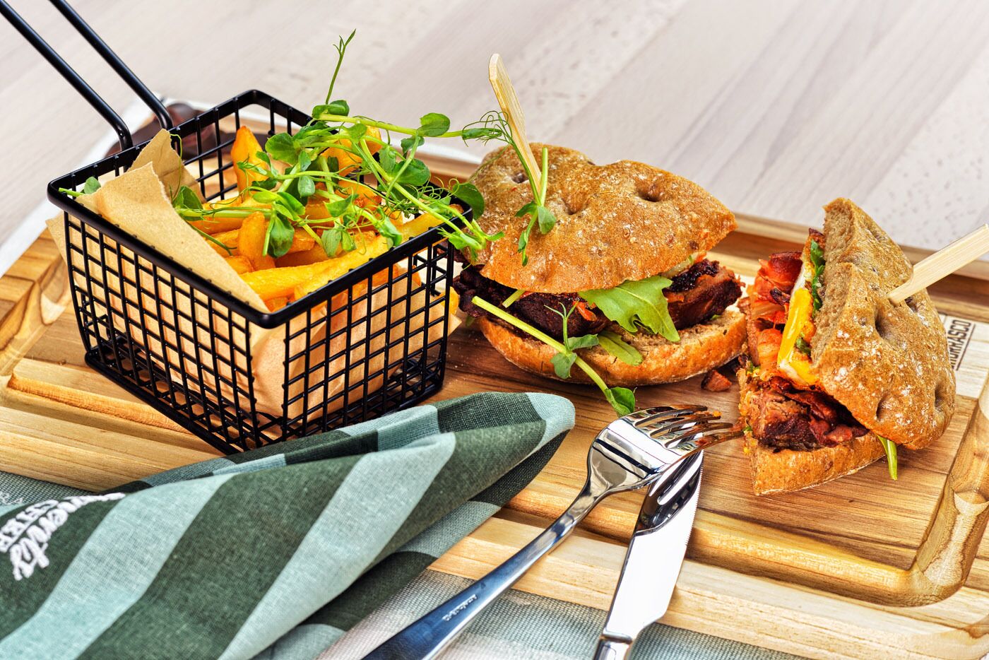 A meal with a burger and fries on a wooden board, a fork, and a knife.
