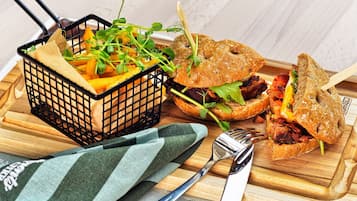 A meal with a burger and fries on a wooden board, a fork, and a knife.