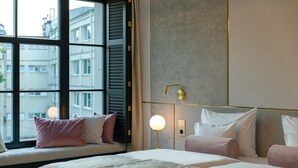 Een hotelkamer met een groot raam, een bed met roze beddengoed en een bedlampje.