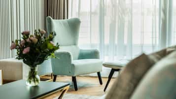 A modern living room with a light blue armchair, a small table with a vase of flowers, and a view through sheer curtains.