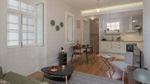 A modern kitchen with white cabinets, a dining area with a table and chairs, and a living space with a sofa and a TV. - Chill Garden Apartment (Funchal)