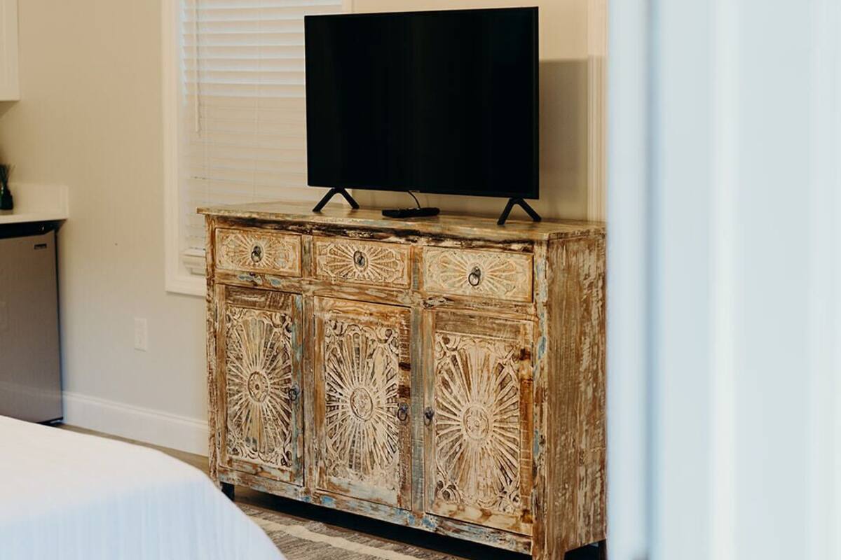 A bedroom with a bed, a television on a wooden cabinet, and a patterned rug.