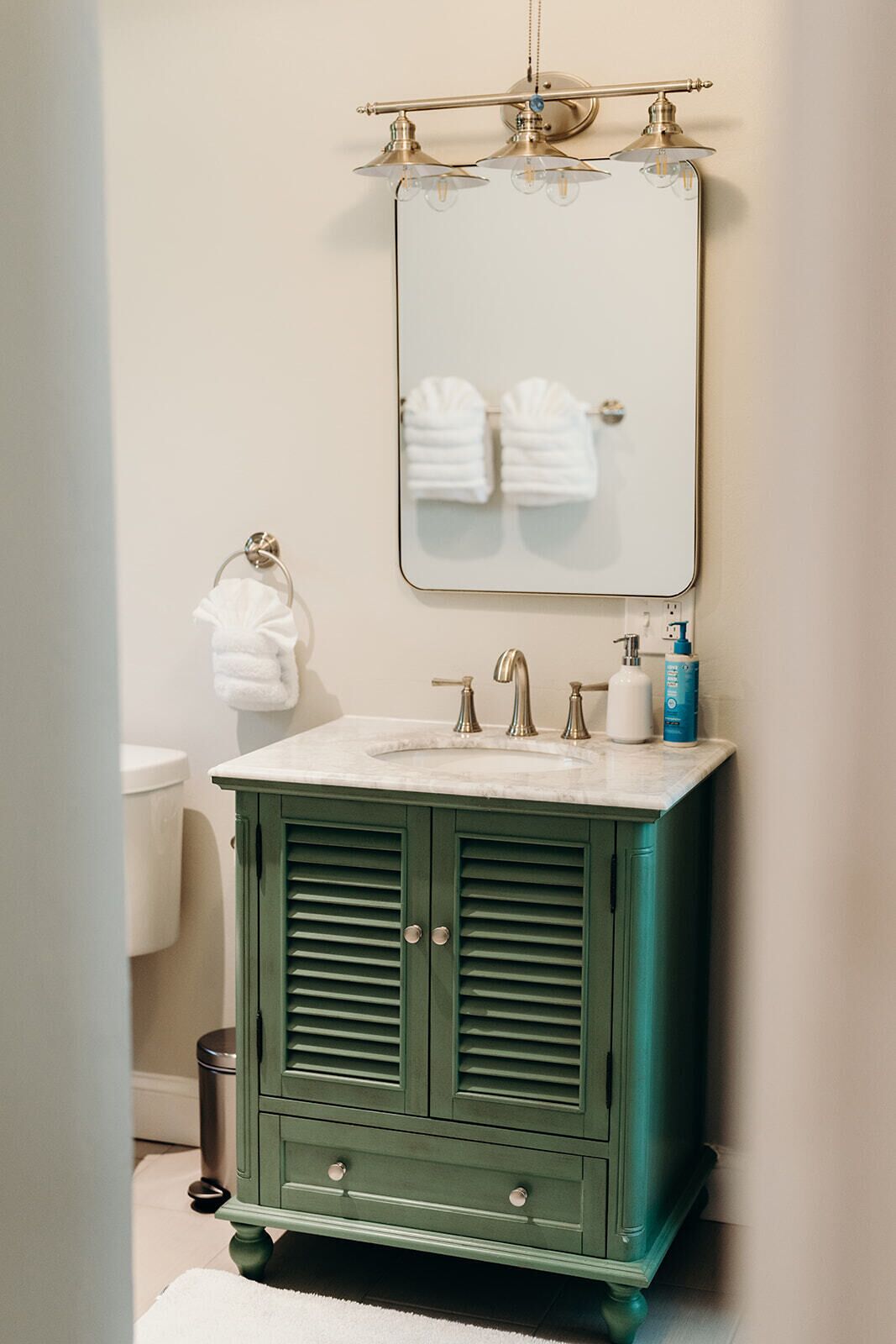 A bathroom with a green vanity, a mirror, two sinks, and a toilet.