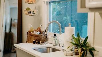 A kitchen counter with a sink, a wicker basket with bottles, a pair of sunglasses, and a bottle of hand soap.