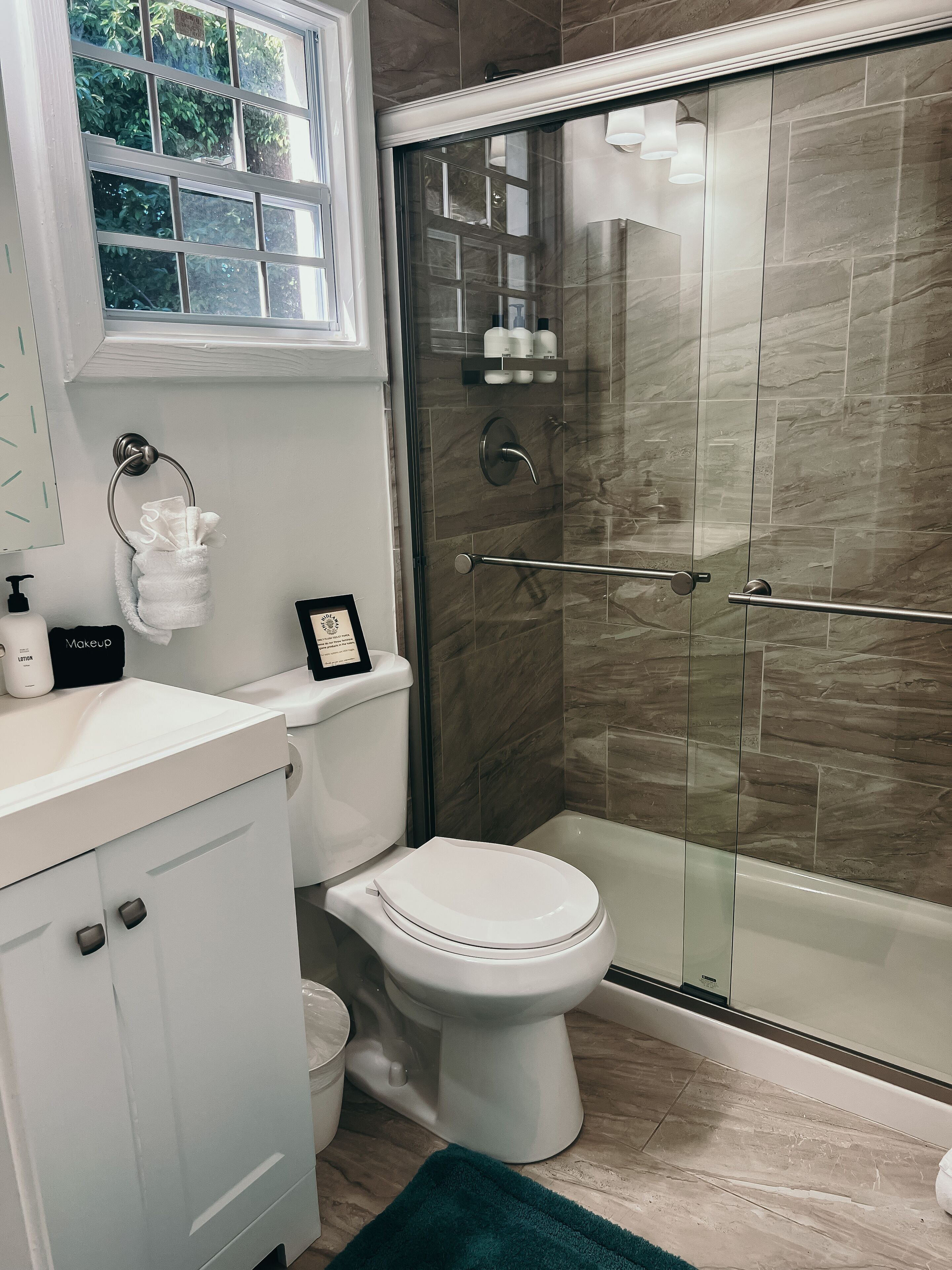 A bathroom with a toilet, a shower with glass doors, and a sink with toiletries.