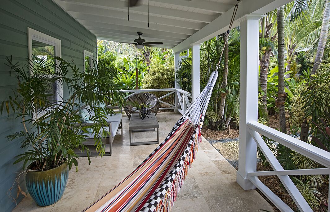 A covered porch with a hammock, potted plants, and a view of tropical vegetation.