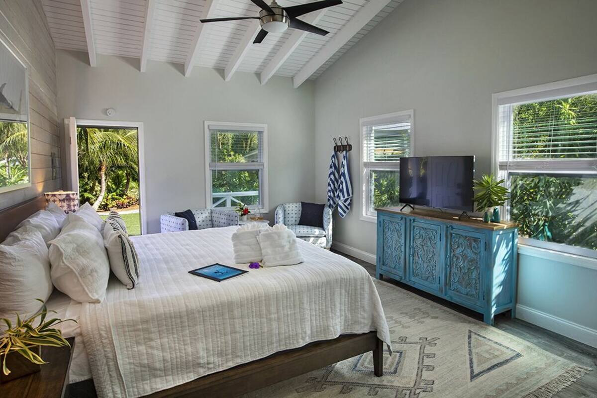 A bedroom with a bed, a TV, a blue cabinet, and large windows.