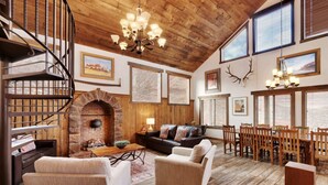 A rustic interior with a stone fireplace, wooden floors, a spiral staircase, and a dining area with wooden chairs and tables. - Hideout at the Rim - Moab's Best Kept Secret (Moab)