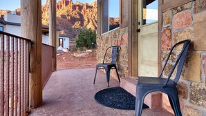 A wooden porch with two chairs, a stone wall, and a view of a mountain range. - Hideout at the Rim - Moab's Best Kept Secret (Moab)
