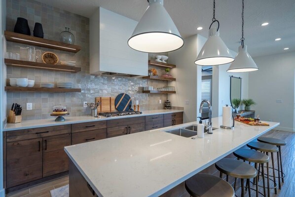 Una cocina moderna con una isla grande, luces colgantes y estantes empotrados.