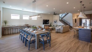 A spacious kitchen with a central island, a dining area with blue chairs, and a staircase leading to an upper level. - Arcadia 71 | Private Hot Tub * Fire Pit * Pool Table * Kid's Nook * Views (Santa Clara)