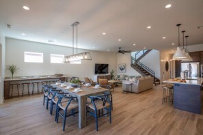 A spacious kitchen with a central island, a dining area with blue chairs, and a staircase leading to an upper level. - Arcadia 71 | Private Hot Tub * Fire Pit * Pool Table * Kid's Nook * Views (Santa Clara)