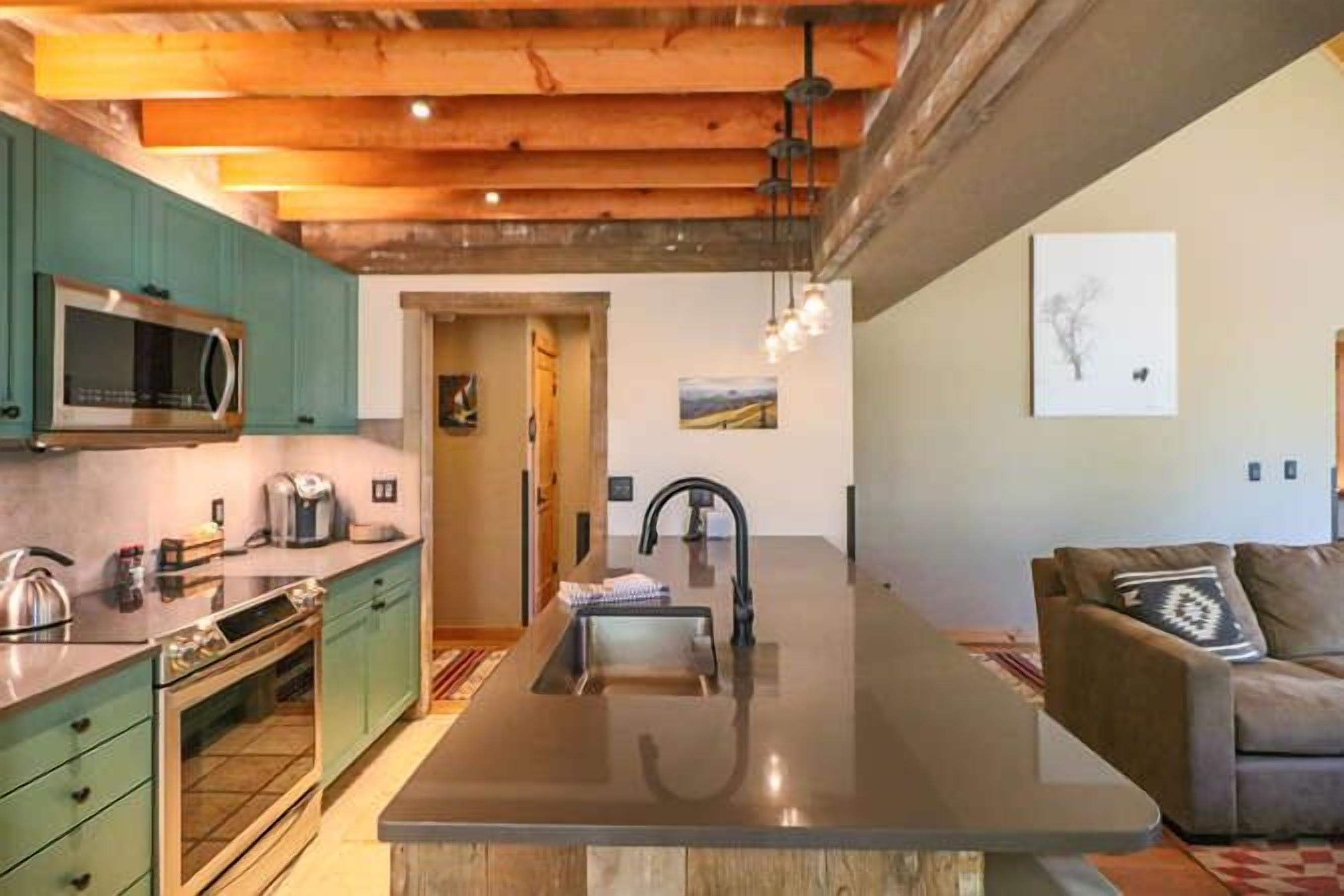 A modern kitchen with a central island, green cabinets, and a large window.