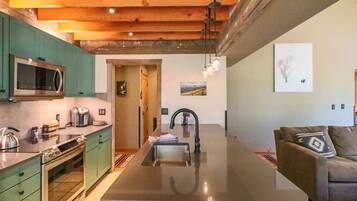 A modern kitchen with a central island, green cabinets, and a large window.