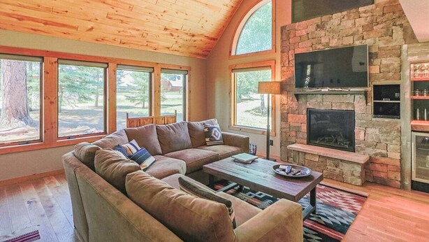 A cozy living room with a stone fireplace, a sectional sofa, and large windows offering a view of the outdoors. - Perfect Family Vacation Getaway! (Pagosa Springs)
