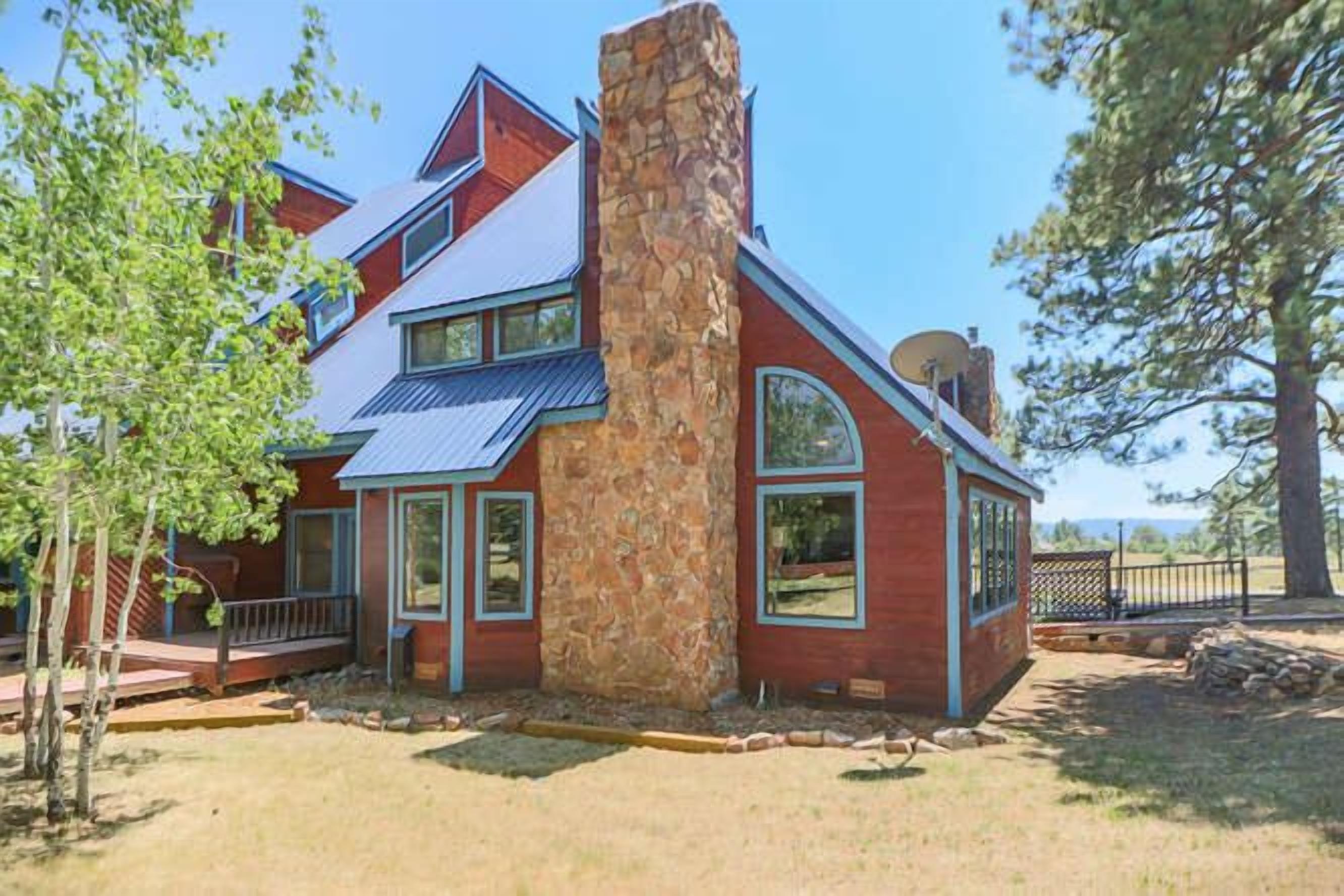 A two-story house with a stone chimney, large windows, and a metal roof.