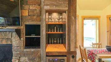 A stone fireplace with a built-in oven, shelves with glassware, and a dining area with a table and chairs.