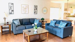 A living room with two sofas, a coffee table, and a side table. There are framed artworks on the wall and a plant on the coffee table. - Magnolia North beautiful vacation condo (Myrtle Beach)