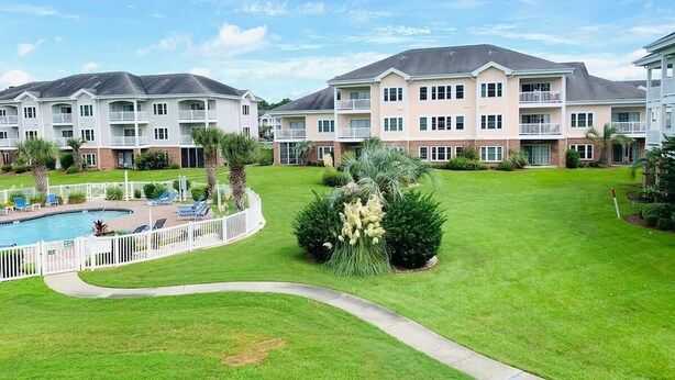A residential building complex with multiple apartment buildings, a swimming pool, and a well-maintained lawn. - Magnolia North beautiful vacation condo (Myrtle Beach)