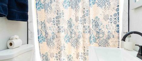 A bathroom with a patterned shower curtain, a toilet, a sink, and towels hanging on the wall.