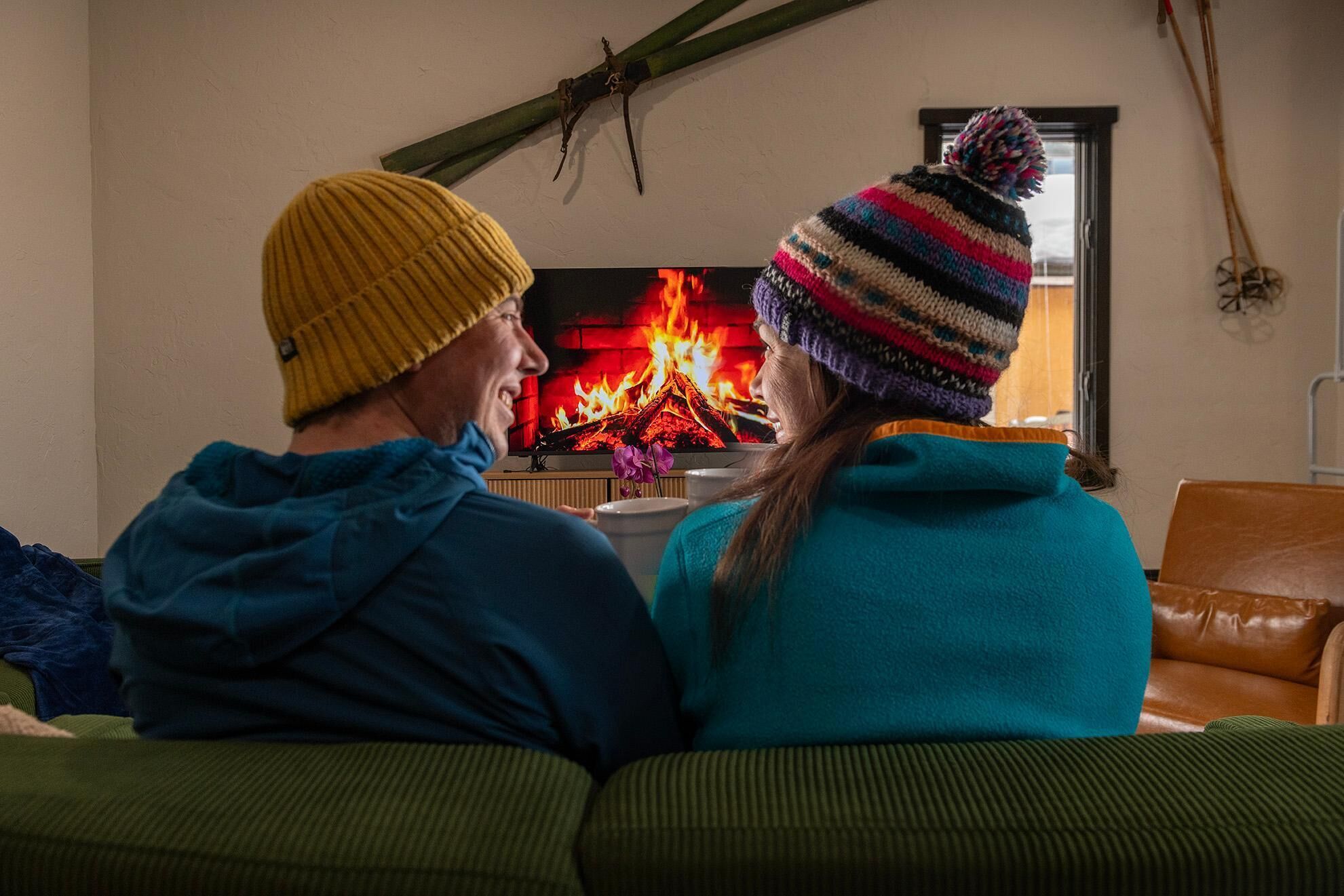 Two people sitting on a couch facing a fireplace with a visible fire.
