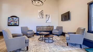 Una sala de estar moderna con sillones tapizados en gris, una mesa de centro de madera y un televisor de pantalla plana grande montado en la pared.