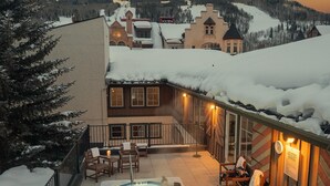 A hot tub with two people, surrounded by wooden deck chairs and a snow-covered landscape. - Lift House Lodge, Pet Friendly Studio Condo (Vail)