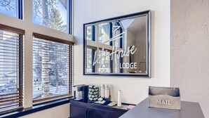 A reception desk with a framed sign reading "Lodge House LODGE", a mail slot, and a coffee station with a coffee maker, cups, and a decorative item. - Lift House Lodge, Pet Friendly, Premium Studio Condo (Vail)