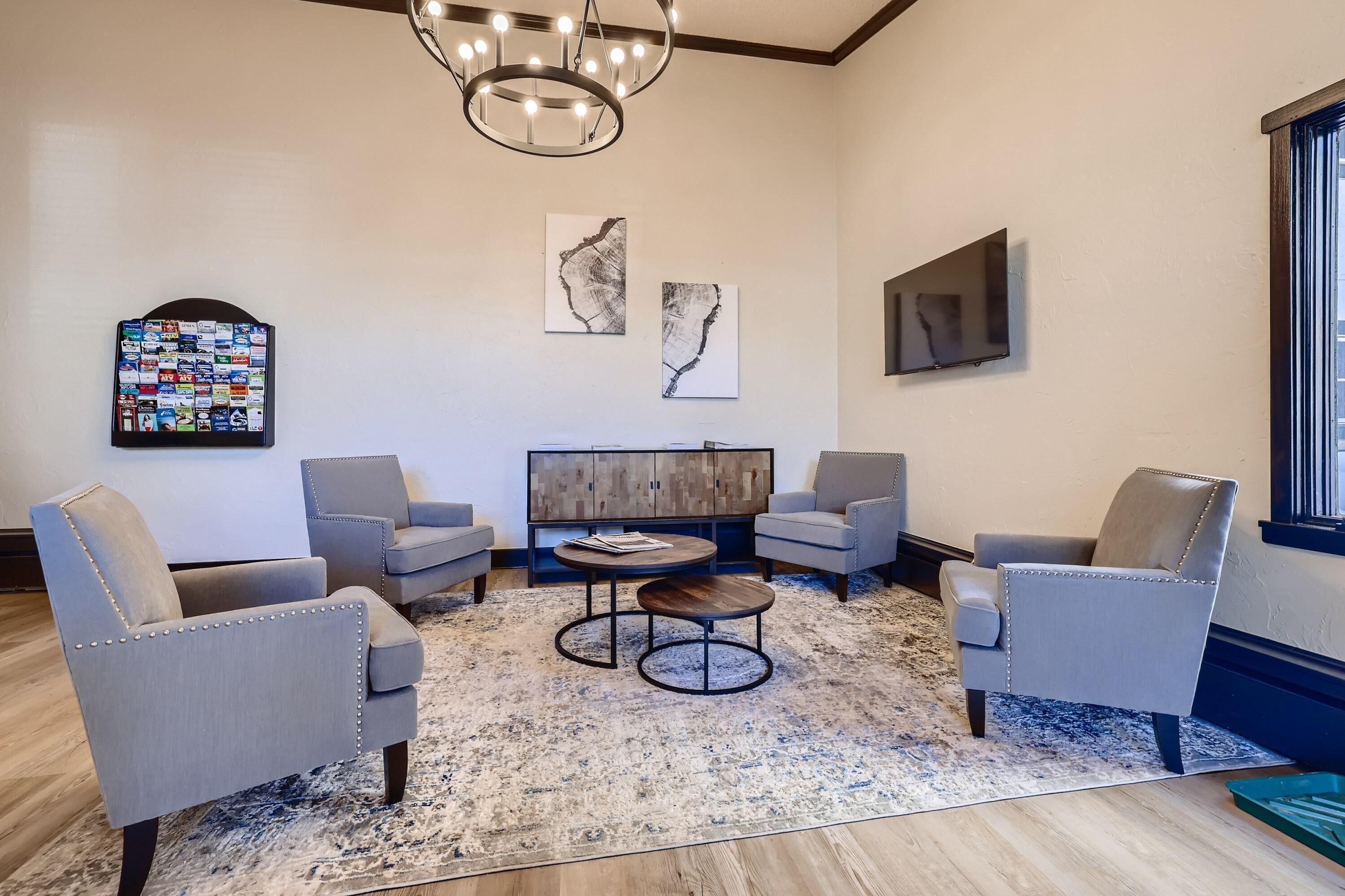 A modern living room with grey upholstered chairs, a wooden coffee table, and a large flat-screen TV mounted on the wall.