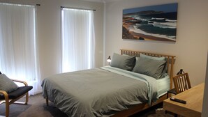 A bedroom with a bed, a chair, a desk, and a painting of a beach scene. - Anglers Rest at Sunderland Bay (Sunderland Bay)