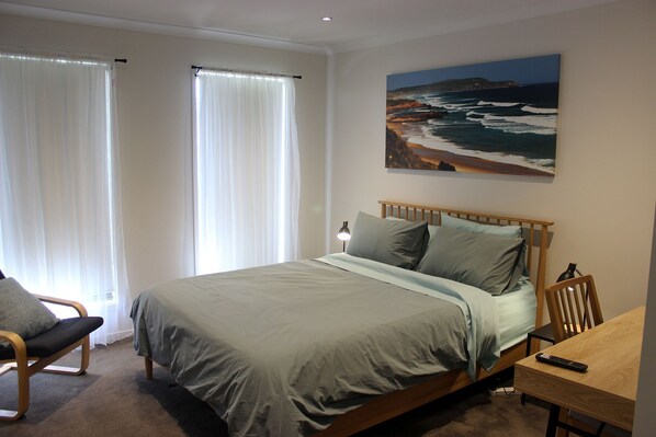 A bedroom with a bed, a chair, a desk, and a painting of a beach scene. - Anglers Rest at Sunderland Bay (Sunderland Bay)