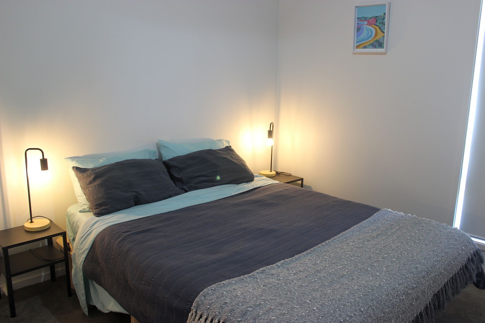 A bedroom with a bed, two bedside tables, a lamp, and a painting on the wall.