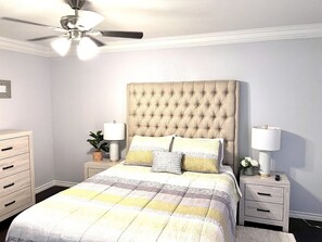 A bedroom with a tufted headboard, a bed with a quilt, two bedside tables with lamps, a nightstand, a dresser, and a ceiling fan. - GP36B | G. Prairie Condo | 3BD | Pool | Workspace (Grand Prairie)