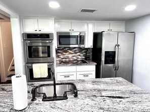 A kitchen with white cabinets, stainless steel appliances, a granite countertop, and a modern faucet.