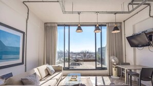 A modern living room with a large window, a sofa, a coffee table, and a TV mounted on the wall. - Homely Studio Apartment in Cape Town (Cape Town)