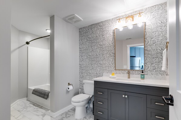 Un baño con ducha, inodoro, tocador y espejo con iluminación.