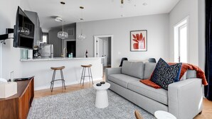 Una sala de estar moderna con un sofá gris, una mesa de centro y una zona de bar con taburetes.