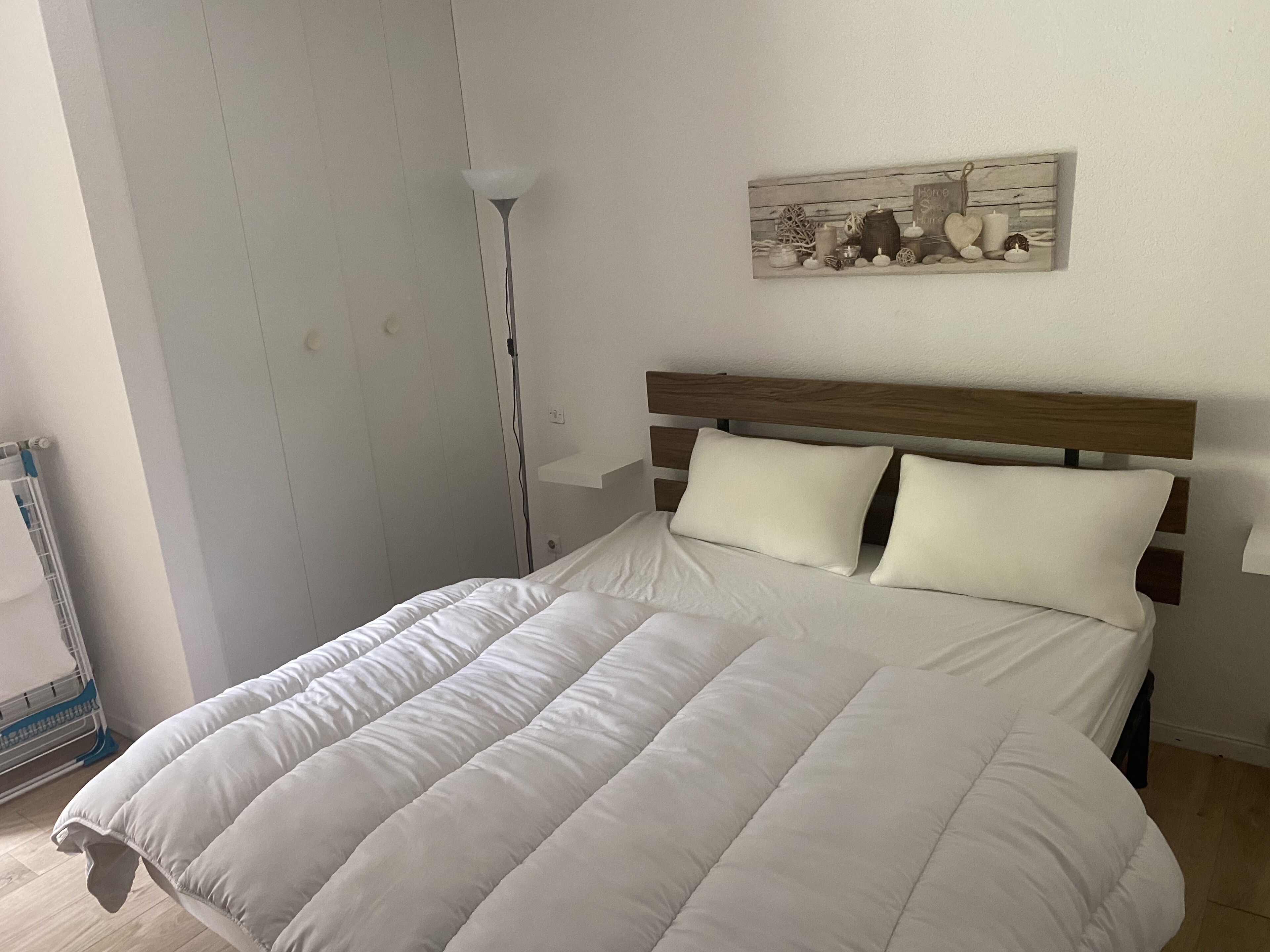 A neatly made bed with a white duvet and pillows, a bedside lamp, and a wall-mounted artwork.