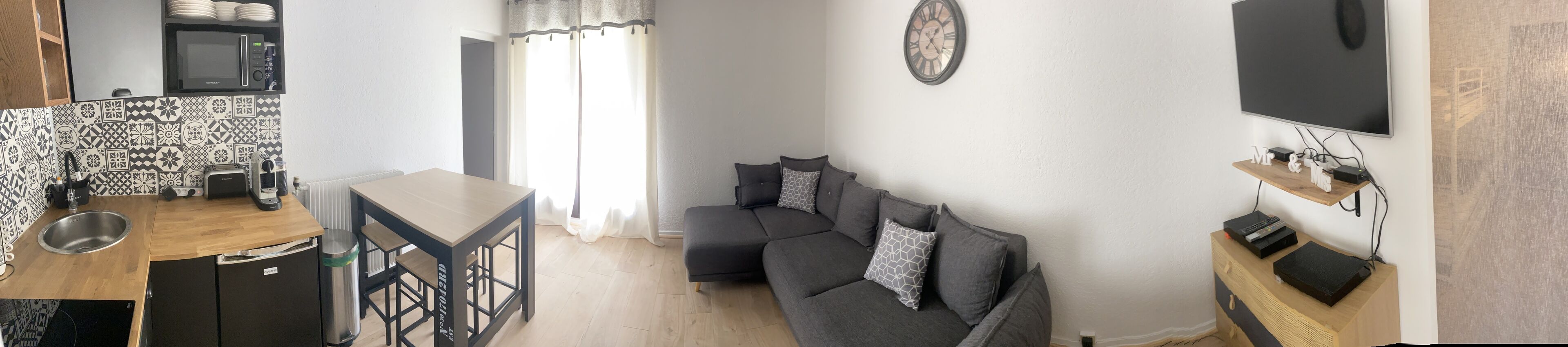 Ein kompakter Wohnraum mit Küchenzeile, einer Couch, einem Flachbildfernseher und einer Wanduhr.