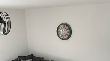 Ein modernes Wohnzimmer mit einem grauen Ecksofa, einer runden Wanduhr und einem Holztisch.